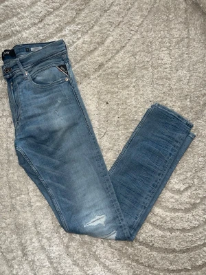 Replay jondrill jeans  - Snygga ljusblåa replay jondrill jeans med fejkhål och slitningar. Jeansen har en slim passform med slitstarkt matrial. Midja 39cm. Längd 107cm. Jag har tyvärr ingen bild när jag bär jeanen på. För bättre inblick i passformen rekommenderar jag att googla på modellnamnet. För storleksguide kolla måtten noggrant då jeansen alltid kan vara uppsydda heller krympta och jag ej tar emot returer :) 1,97