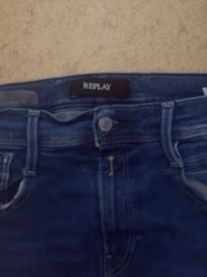 Blå jeans från Replay - Säljer ett par klassiska blå jeans från Replay med normal midja och raka ben. Jeansen har fem fickor, bälteshällor och är tillverkade i en mjuk bomullsblandning med lite stretch för extra komfort. Perfekta för en avslappnad och snygg look.