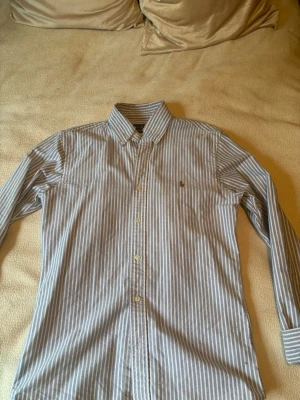 Randig blå skjorta Ralph Lauren slim - Säljer en klassisk blå och vit randig skjorta från Ralph Lauren i slim fit. Tillverkad i mjuk bomull