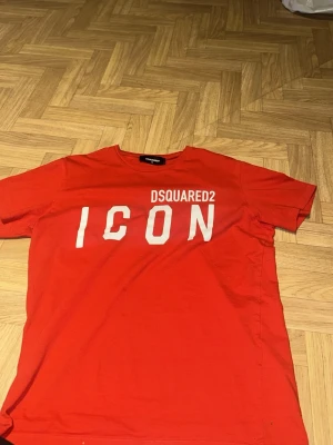 dsquared 2 icon tshirt - Snygg röd t-shirt från Dsquared2 med stort vitt 'ICON'-tryck på bröstet och klassisk rund hals. T-shirten är köpt i italien när jag va på resa dit år 2022 på min födelsedag den är helt som ny för jag inte anvönt den eftersom jag inte tycker om förgen om ni ha frågar kom dm priset kan diskuteras