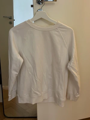 Vit basic sweatshirt XS - En enkel vit sweatshirt i storlek XS med rund halsringning och ribbade muddar vid ärmslut och nederkant. Tröjan har en avslappnad passform och är tillverkad i mjukt material, perfekt för en clean och stilren look.