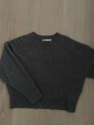 Mörkgrå stickad tröja från Zara - Mysig mörkgrå stickad tröja från Zara med rund halsringning och ribbade muddar vid ärmslut och nederkant. Tröjan har en avslappnad passform och är perfekt för lager på lager. Materialet känns mjukt och värmande.