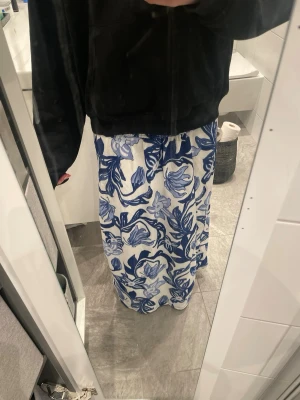 Vit långkjol med blått blommönster - Somrig och elegant vit långkjol med ett vackert blått blommönster som jag sytt själv. Tyget faller mjukt och ger en avslappnad men stilren look som funkar både till stranden, stan och vardagsoutfits. Den har en bekväm resår i midjan. Midjemåttet är 70 cm, dvs storlek XS/S, men på grund av resoren så passar den även större storlekar.
