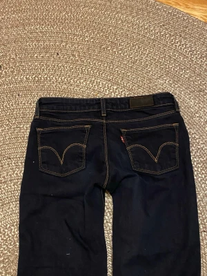 Mörkblå Levi's 572 jeans bootcut - Svarta/mörkblå. De är lite dammiga på bilderna men jag kommer tvätta dem innan de skickas. Midjan rakt över:34cm. Innerben: 76cm