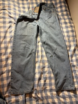 Blå raka jeans från Wrangler, strl 32 - Säljer ett par klassiska blå jeans från Wrangler i rak modell. Jeansen har fem fickor, gylf med knapp och dragkedja samt snygga kontrastsömmar. Tillverkade i slitstark denim som passar perfekt till en avslappnad stil.