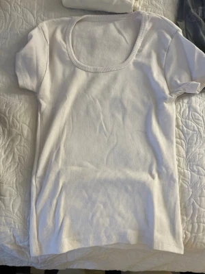 Vit ribbad topp med kort ärm - En enkel och stilren vit ribbad topp med korta ärmar och rundad urringning. Perfekt att matcha med jeans eller kjol för en clean look. Mjuk och stretchig känsla.