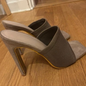 Bruna slip-in klackskor i mocka-look - Bekväma beigebruna slip-in pumps med bred ribbad textil över foten och öppen tå. Skorna har fyrkantig tå och hög klack i mocka-liknande material. Aldrig använda.