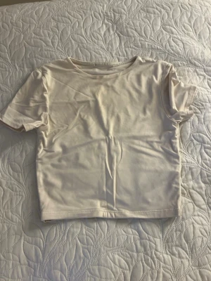 Ljusbeige croppad t-shirt - En enkel och stilren ljusbeige croppad t-shirt med rund hals och korta ärmar. Perfekt basplagg i garderoben, tillverkad i mjuk bomull för en skön känsla. Passar till allt och är lätt att matcha med olika stilar.