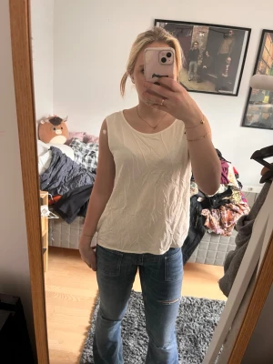 Vit ärmlös linnetopp - Säljer en enkel och stilren vit linnetopp med rund halsringning. Toppen är ärmlös och har en avslappnad passform, perfekt att matcha med jeans eller kjol. Inga synliga detaljer eller mönster, bara clean och fräsch look.