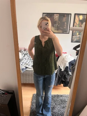 Grön spetslinne med v-ringning - Snyggt grönt linne med v-ringad hals och spetsdetaljer. Ärmlös modell som passar perfekt till jeans eller kjol. Luftigt och stilrent plagg för dig som gillar en enkel men trendig look.