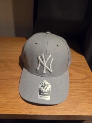 Grå New York Yankees keps från '47 - Snygg grå keps från '47 med New York Yankees-logga broderad framtill. Justerbar passform med klassisk böjd skärm och ventilation. Perfekt för dig som gillar sportiga accessoarer och streetstyle. Materialet är slitstark bomull. Helt ny. 