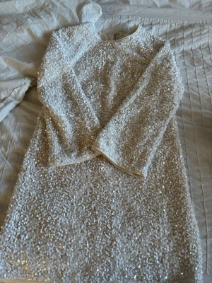 Vit paljettklänning med lång ärm XS - Supersnygg vit klänning täckt med paljetter och lång ärm. Klänningen har rund halsringning och dragkedja i ryggen. Perfekt för dig som vill sticka ut med ett glittrigt plagg. Fodrad för extra komfort och sitter snyggt på kroppen.