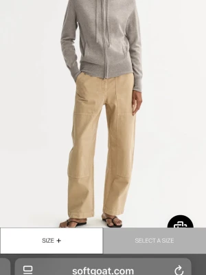 Grå zip-hoodie i cashmere Soft Goat - Snygg grå zip-hoodie från Soft Goat i mjuk cashmere. Tröjan har huva med dragsko, två fickor fram och ribbade muddar vid ärmslut och nederkant. Perfekt för en avslappnad och stilren look. I färgen greige.