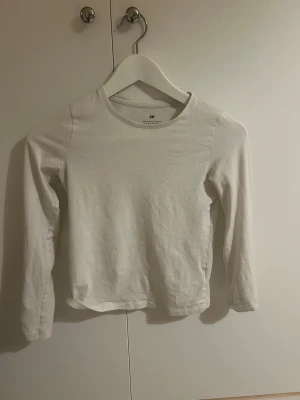 Vit långärmad topp från H&M - En basic vit långärmad topp från H&M med rund halsringning. Tillverkad i mjukt bomullsmaterial och har en enkel, rak passform som passar till det mesta. Perfekt att styla lager på lager eller bära som den är. Skriv vid frågor 💕💕