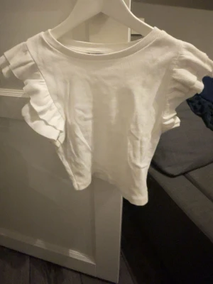 Vit volangtopp från Zara - Supersöt vit topp från Zara med volangdetaljer på ärmarna. Toppen är ribbad och har en rund halsringning. Perfekt att styla med jeans eller kjol för en trendig look. Har även en likadan i svart om någon är intresserad! 75kr för 1 och 2 för 100