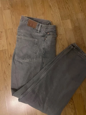 Grå raka jeans med hög midja - Säljer ett par grå blåa jeans med rak passform och hög midja. Klassisk femficksmodell med bälteshällor och knappgylf. Jeansen är i ett tjockare denimtyg och har en stilren look som passar till det mesta. Dessa är i storlek 30/34
