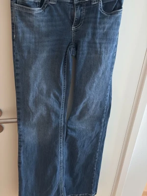 Blå bootcut jeans med kontrastsömmar - Säljer ett par klassiska blå jeans med kontrastsömmar. Jeansen har fem fickor och låg midja. Perfekta till en avslappnad stil och passar till det mesta. Materialet är mjukt denimtyg.