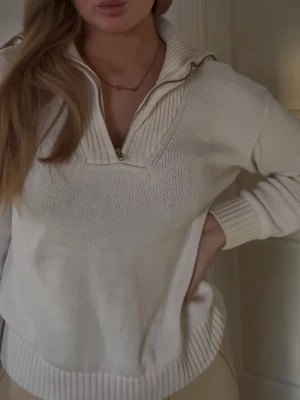 Vit stickad tröja med dragkedja Zara - Beige stickad tröja från Zara med hög krage och dragkedja framtill. Tröjan har ribbade detaljer vid krage, ärmslut och nederkant. Perfekt för lager på lager och en avslappnad men stilren look.