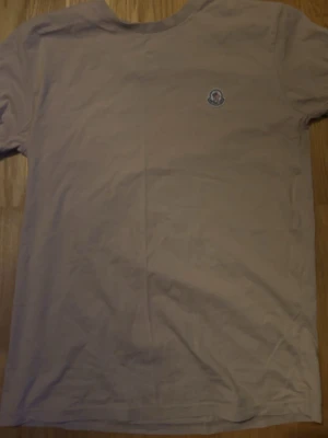 Beige t-shirt från Moncler - Snygg beige t-shirt från Moncler med liten logga på bröstet. Klassisk rund halsringning och korta ärmar. Perfekt basplagg för en clean och stilren look.
