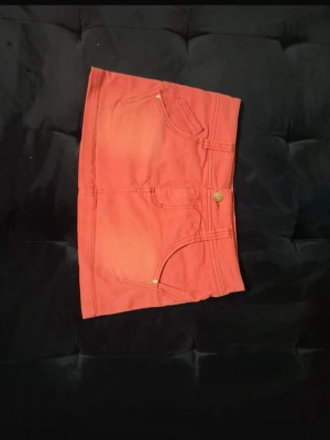 Kort jeanskjol med fickor - Snygg rosa kortkjol med klassisk jeanslook och framfickor. Kjolen har knapp och dragkedja framtill samt detaljer i guld. Perfekt för dig som vill ha en enkel men trendig stil. Den är mer rosa i verkligheten än på bild