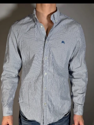 Randig skjorta från Gant - Klassisk skjorta från Gant med smala blå och vita ränder, button-down krage och broderad logga på bröstet. Tillverkad i bomull och har långa ärmar med manschetter. Perfekt för en clean och stilren look.
