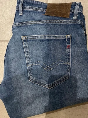 Blå raka jeans från Replay - Säljer ett par klassiska blå jeans från Replay med raka ben och snygga slitningar. Jeansen har fem fickor, tydliga sömmar och Replay-logga på bakfickan. Perfekta för en avslappnad och trendig look.