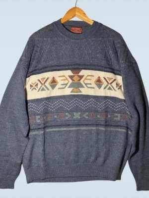 Hillman Classics Blå stickad tröja med mönster XL - Säljer en blå stickad tröja från Billabong med retro mönster i beige, grönt, brunt och orange över bröstet. Tröjan har rund hals, långa ärmar och ribbade muddar. Perfekt för dig som gillar vintagevibbar och snygga detaljer.