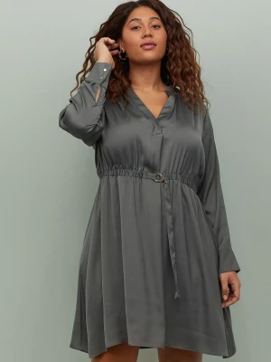 Grå kort klänning med bälte - Säljer en snygg grå kort klänning med v-ringning och långärmar. Klänningen har ett bälte i midjan med metallspänne och är tillverkad i ett glansigt material som ger en elegant look. Perfekt för dig som gillar stilrena plagg med detaljer.