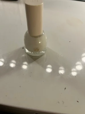 Vitt nagellack från H&M - Snyggt vitt nagellack från H&M i en rund glasflaska med beige lock. Perfekt för en fräsch och stilren look på naglarna. Lätt att applicera med den smidiga borsten och ger ett jämnt resultat.