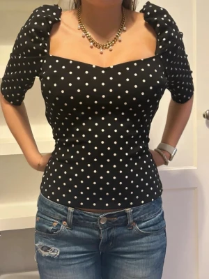 Svart prickig topp med puffärmar - Snygg svart topp med vita prickar och puffiga korta ärmar. Toppen har en fyrkantig urringning och figurnära passform som ger en trendig siluett. Perfekt att styla med jeans eller kjol för en cool look.