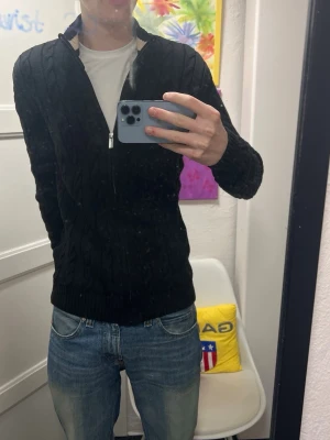 Nästan oanvänd kabelstickad ziptröja - Säljer en svart kabelstickad tröja med dragkedja framtill och hög krage. Tröjan har ribbade muddar vid ärmslut och nederkant, vilket ger en snygg och tajt passform. Perfekt för dig som gillar en stilren och enkel look.