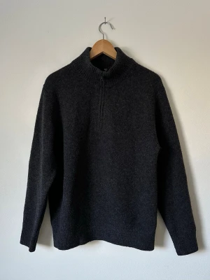 Mörkgrå Uniqlo stickad halvzip tröja - Mysig mörkgrå stickad tröja med halv dragkedja och hög krage. Tröjan har en avslappnad passform, långa ärmar och ribbade muddar vid ärmslut och nederkant. Perfekt för lager på lager och enkel att matcha med olika stilar.