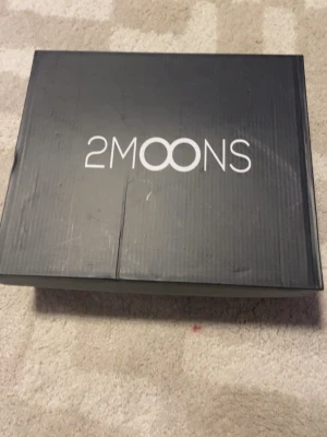 Bruna uggs från 2MOONS - Säljer ett par snygga bruna uggs från 2MOONS. De har en klassisk slip-on design med mjukt mockaliknande material och grov sula för extra komfort. Perfekta för att hålla fötterna varma hemma eller när du vill chilla.