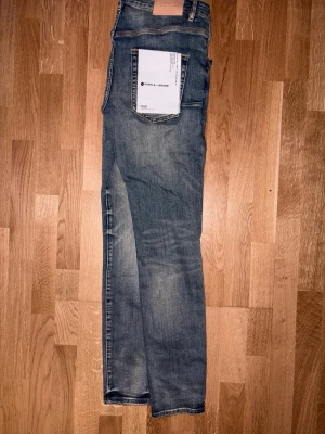 Blå Purple jeans - Säljer ett par blå skinny jeans från purple med see through slitningar och tvättade detaljer på framsidan. Jeansen har klassisk femficksmodell, knappgylf och smal passform. Har tagg Purple som man kan få med också!