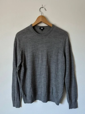 Grå stickad tröja från Uniqlo - Klassisk grå stickad tröja från Uniqlo i mjuk merinoull. Tröjan har rund halsringning, långa ärmar och ribbade muddar vid ärmslut och nederkant. Perfekt basplagg för lager på lager och enkel att matcha med olika stilar. 8D18