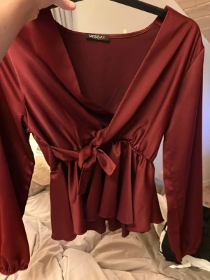 Vinröd omlottblus med knytband - Stilren vinröd omlottblus från Missay med långa ärmar och volang nedtil. Endast använd 1 gång.