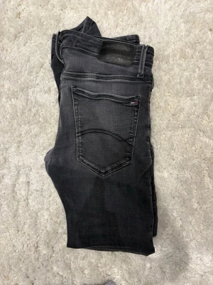 Svarta skinny jeans från Tommy Hilfiger - Säljer ett par svarta skinny jeans från Tommy Hilfiger med klassisk femficksdesign och diskret logga på bakfickan. Jeansen har en tight passform och är tillverkade i stretchigt denimtyg för extra komfort.