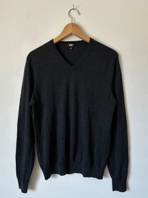Mörkgrå V-ringad stickad tröja Uniqlo - Klassisk mörkgrå stickad tröja från Uniqlo med V-ringning och långa ärmar. Tillverkad i tunt, mjukt material som passar perfekt för lager på lager. Ribbstickade muddar vid ärmslut och nederkant ger en snygg passform. 8D23