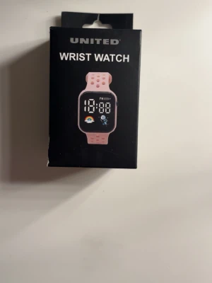 Rosa digital klocka från United - Digital armbandsklocka från United med rosa silikonarmband och svart display. Klockan har tid- och datumfunktion samt en färgglad ikon på skärmen. Perfekt för dig som gillar en sportig och modern stil.