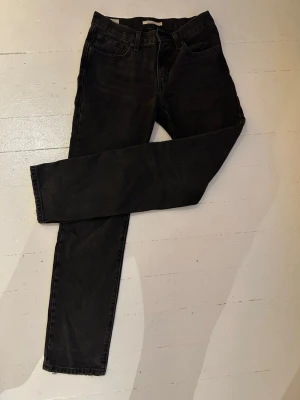 Svarta Levi’s Middy Straight jeans - Säljer ett par svarta Levi's jeans i modellen Middy Straight. Klassisk femficksdesign, dragkedjegylf och raka ben. Jeansen är tillverkade i ett slitstarkt denimtyg i 100% bomull och har en tidlös look som passar till allt. Storlek: W27 L33.