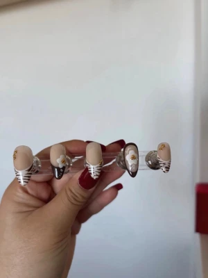 Bruna och vita press-on naglar med mönster - Snygga press-on naglar i mandelform med beige bas, bruna och vita zebramönster, guldiga stenar och blommor som dekoration. Perfekt för dig som vill ha en trendig och unik look. Gjorda i slitstarkt plastmaterial.