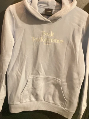 Ljusblå hoodie Peak Performance - Snygg ljusblå hoodie från Peak Performance med broderad logga framtill. Klassisk känguruficka och huva. Perfekt för en avslappnad och sportig stil. Mjuk bomullskänsla och ribbade muddar vid ärmslut och nederkant.