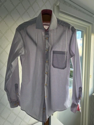 Rutig skjorta från Seven Seas M - Klassisk rutig skjorta från Seven Seas i vitt med tunna blå och röda rutor. Skjortan har lång ärm, bröstficka och knappar framtill. Tillverkad i strykfri bomull för extra bekvämlighet. Perfekt för en clean och stilren look.