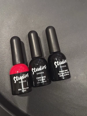 Studios Didier gel nagellack 3-pack - Säljer ett 3-pack gel nagellack från Studios Didier. Innehåller en stark röd färg, en fiber base och ett super shiny top coat. Alla flaskor är på 8 ml och har klassisk rund form med svart lock. Perfekt för dig som vill fixa snygga naglar hemma.