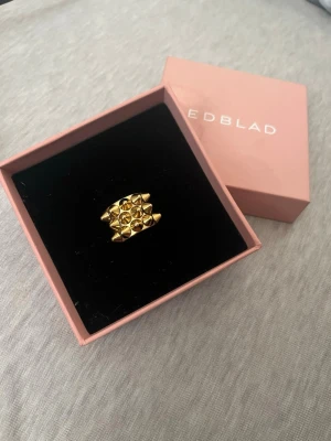 Guldfärgad ring från Edblad spike ring  - Snygg guldfärgad ring från Edblad med cool pyramidformad design. Ringen har flera små, upphöjda trianglar som ger ett unikt och trendigt uttryck. Perfekt accessoar för dig som gillar statement-smycken och vill sticka ut lite extra. I storlek 16,00 och väldigt bra skick där boxen kommer med och original priset är 400 men är för liten så hann ej användas 