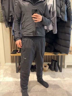 Svart Nike träningsset herr - Säljer ett svart träningsset från Nike med zip-jacka och matchande byxor. Jackan har dragkedja framtill och hög krage, byxorna har resår i midjan och diskret Nike-logga på benet. Perfekt för gymmet eller löprundan. BYXORNA ÄR I STORLEK M OCH JACKAN I STORLEK S!!