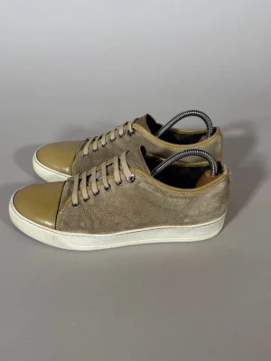Beige sneakers med mocka och gummitå - Snygga beige sneakers med ovandel i mocka och tåparti i glansigt gummi. Skorna har vita sulor och matchande beige skosnören. Perfekta för en avslappnad och trendig stil.