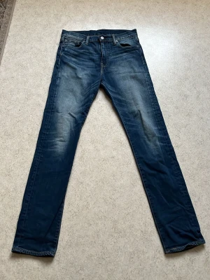 Blå Levi's jeans med slitningar - Säljer ett par klassiska blå Levi's jeans med snygga slitningar och tvättade detaljer. Jeansen har fem fickor, raka ben och en ikonisk läderpatch bak i midjan. Perfekta för en avslappnad och trendig stil. Modellen är 510 och storleken är W30 L32.