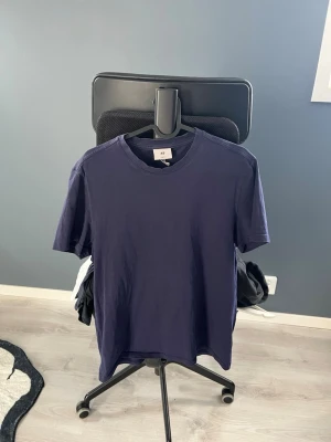 Mörkblå t-shirt från H&M - En enkel och stilren mörkblå t-shirt från H&M. Klassisk rund halsringning och korta ärmar. Perfekt basplagg i garderoben, tillverkad i mjuk bomull för skön komfort.