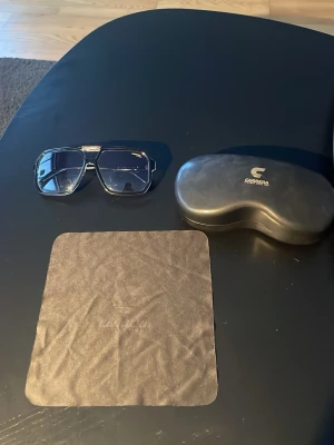 Svarta Carrera pilotbågar solglasögon - Fräscha svarta solglasögon från Carrera med klassisk pilotform och mörkblå tonade glas. Bågarna är i plast och har Carrera-logga på skalmen. Kommer med originalfodral och putsduk. Använt ett fåtal gånger.